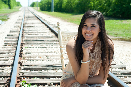 Attractive teen girl sitting on an old chair on railroad tracks.