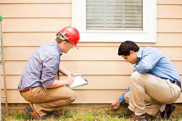Inspectors or blue collar workers examine building wall, foundation. Outdoors. Repairmen, building inspectors, exterminators, engineers, insurance adjusters, or other blue collar workers examine a building/home's exterior wall and foundation. One wears a red hard hat and clear safety glasses and holds a clipboard. The other checks the foundation with tool. inspector stock pictures, royalty-free photos & images