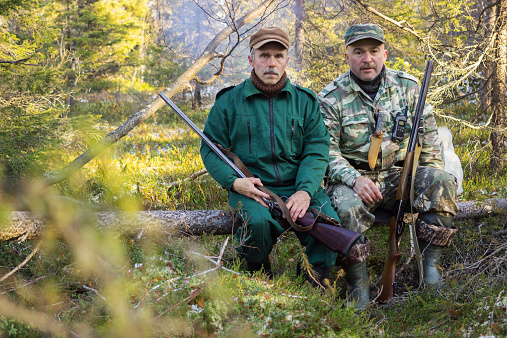 Two older hunters rest, sitting on a log