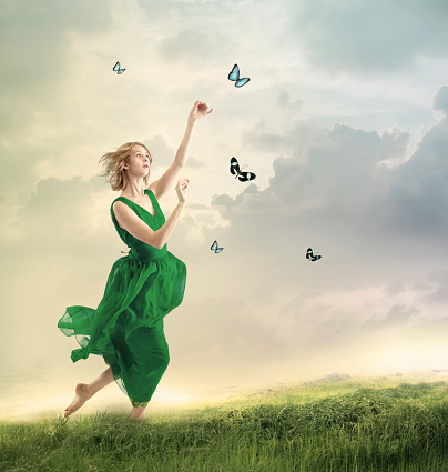Beautiful girl in a green dress following butterflies on a mountain