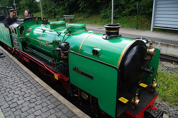 Dresden, Germany - July 11, 2014: Dresden Park Railway, steam locomotive number 1 (Lisa) standing at a platform in a railway station, with two drivers sitting in the open cockpit of the steam train.