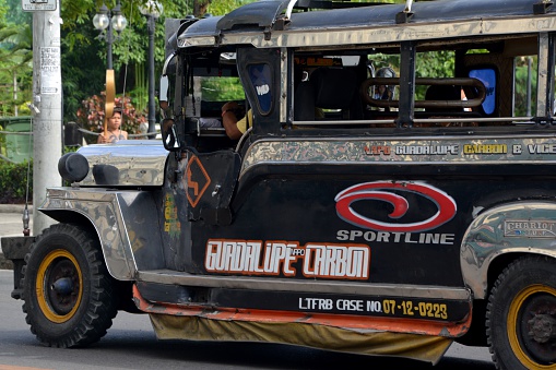 Cebu City, Philippines - February 10, 2014: Hot Rod black Jeepney riding on Cebu City old downtown streets. In the background a filipino guy walking aside the road.