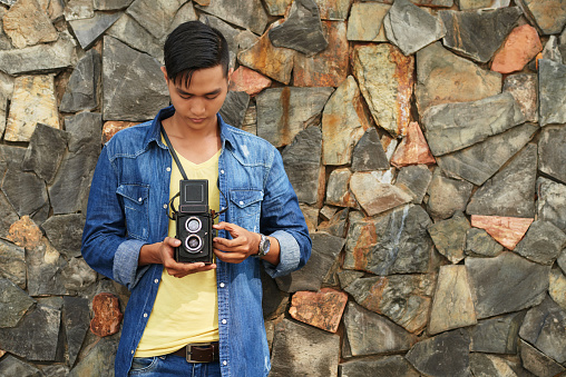 Asian young man with retro camera standing at stone wall