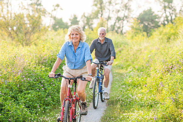 montar bicicletas en un seguimiento un través de un campo - action mature adult bicycle senior couple fotografías e imágenes de stock