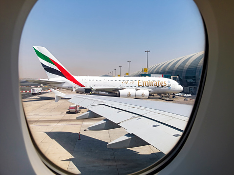 Dubai, UAE - August 9, 2015: As one Emirates Airbus A380 departs busy Dubai Airport, a similar aircraft in the next bay (F19) is framed in the passenger window as it is being prepared for its next flight.