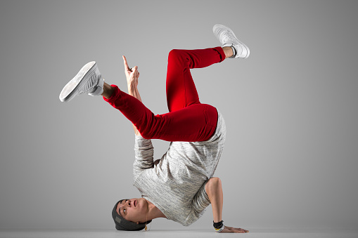 One fit young man in casual red jeans working out, performing breakdance moves on the floor. Full length photo on studio gray background