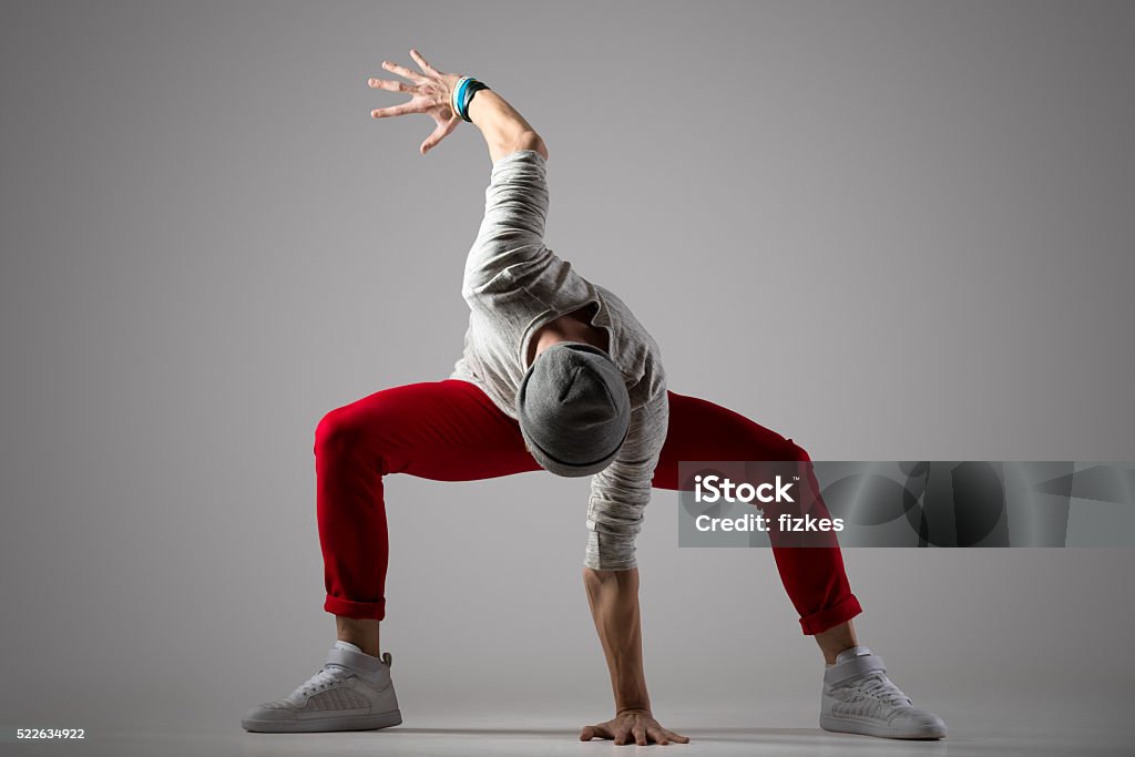 Cool street style dancer One sporty cool young man in casual red pants and beanie working out, dancing. Street style dancer performing. Full length photo on studio gray background Dancing Stock Photo