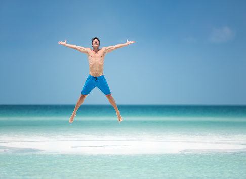 Handsome man in bathing shorts jumping at a secluded tropical Beach.
