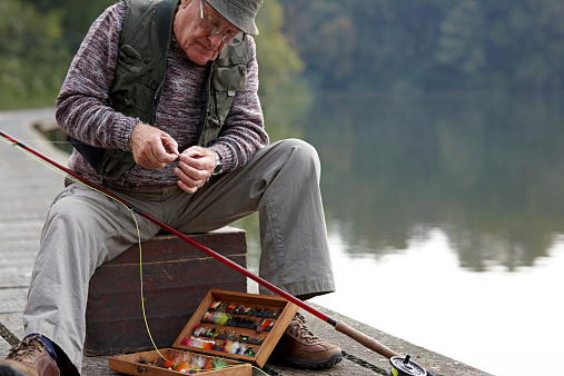 Senior man selecting the right lure from tackle box preparing the bait for fishing by the lake