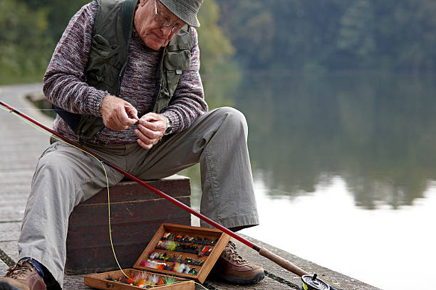 Senior man preparing the bait for fishing Senior man selecting the right lure from tackle box preparing the bait for fishing by the lake fishing bait stock pictures, royalty-free photos & images