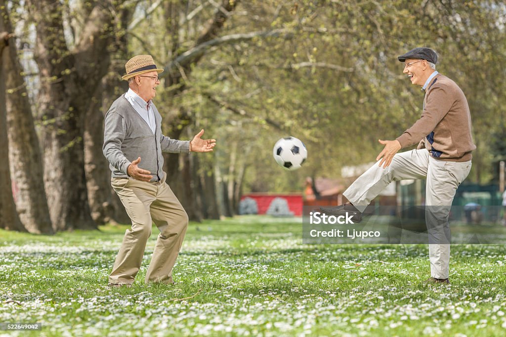 Two joyful seniors playing football in a park Two joyful seniors playing football in a park on a beautiful spring day Senior Adult Stock Photo