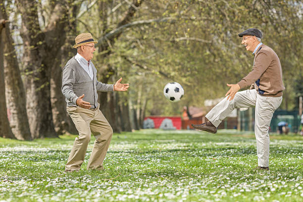 две счастливые пожилых людей играть в футбол в парке - pass the ball стоковые фото и изображения