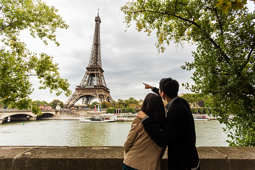 Sightseeing Young Asian couple on a romantic vacation pointing towards the Eiffel Tower in Paris