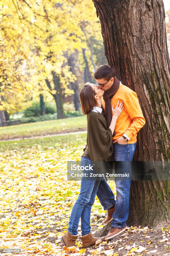 Couple kissing in beautiful autumn park A young woman kissing a guy in a park on a sunny autumn day while he was leaning against a tree. 20-29 Years Stock Photo