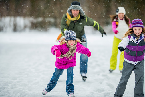 A family ice-skating on a frozen pond on a snowy day.
