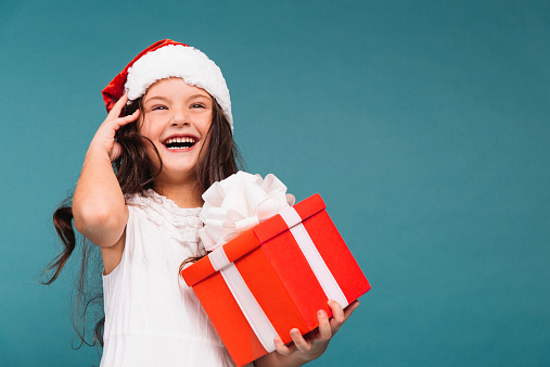 Little girl in santa costume playing with santa head in front of white background.