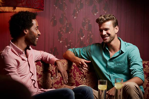 Happy friends communicating on sofa at nightclub Happy young male friends communicating while relaxing on sofa at nightclub black men with blonde hair stock pictures, royalty-free photos & images