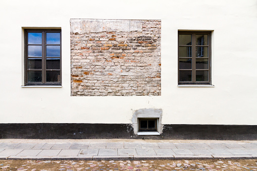 Modern white street wall with some small windows and example of old brickwork