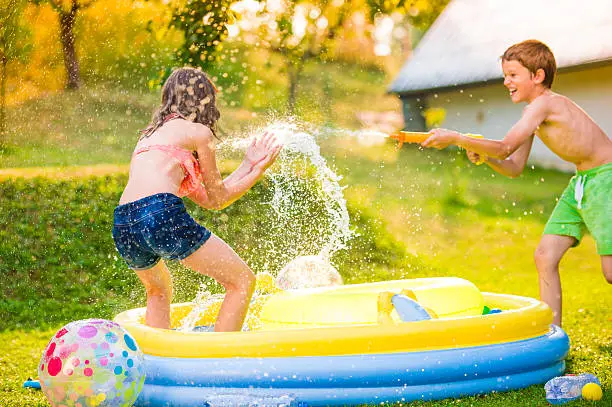 Photo of Boy splashing girl with water gun, garden swimming pool
