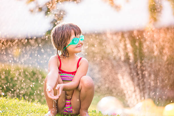 istock Cute girl crouching under the water splashing from sprinkler 522736638