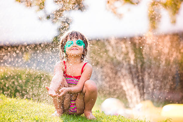 istock Cute girl crouching under the water splashing from sprinkler 522736728