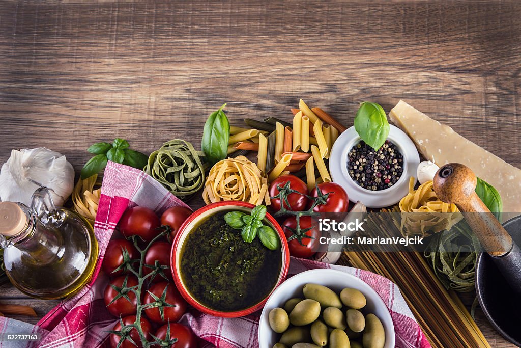 Italian and Mediterranean food ingredients on old wooden background. Italian and Mediterranean food ingredients on old wooden background.Spaghetti olives basil pesto tomato pasta garlic pepper olive oil and mortar. Backgrounds Stock Photo