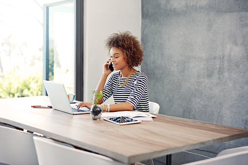 Shot of a young woman talking on the phone while working at her desk at home