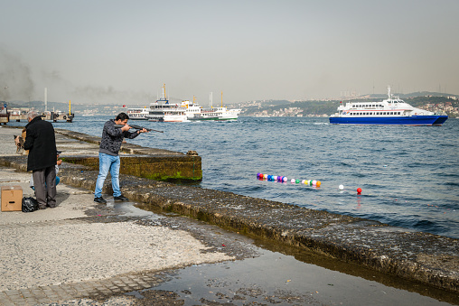 Istanbul, Turkey - April 08, 2016: Man is shooting balloons on the water of Bosphorus in Istanbul, Turkey
