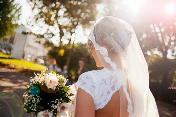 Beautiful bride holding flower bouquet view from back, lens flare
