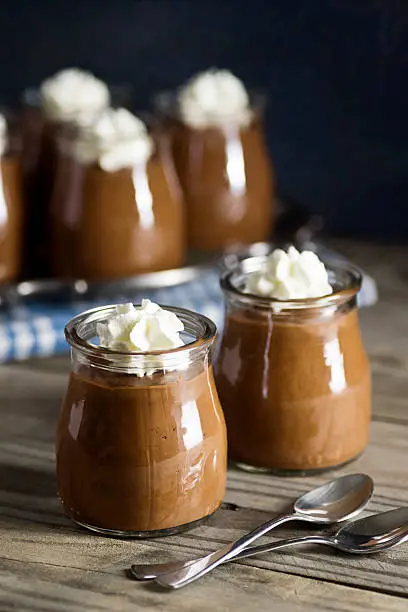 Homemade chocolate pudding topped with whipped cream in little glass cups on a wooden table.
