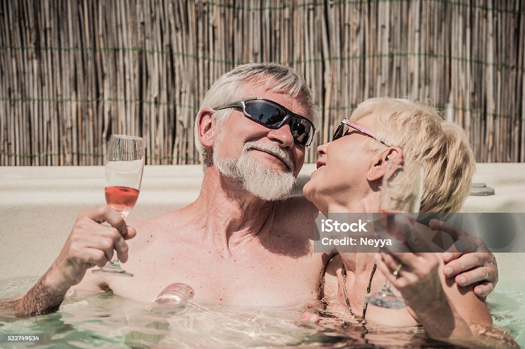 Cheerful Senior Couple Enjoying Summer Vaccation in hot tub Senior couple embracing and drinking sparkling wine in hot tub on the summer terrace. She has blond short hair and he has gray hair and beard. Boath wearing sunglasses and smiling to each other. Portorož, Slovenia, Europe. 60-69 Years Stock Photo