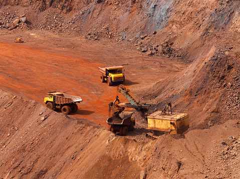 Quarry excavator load the iron ore to big dump truck in openpit mine with another two trucks waiting in queue