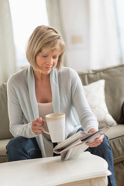 istock Woman Holding Coffee Mug While Reading Newspaper On Sofa 522763297