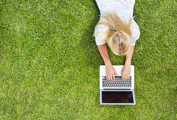 en línea en el parque - lying down women laptop freedom fotografías e imágenes de stock