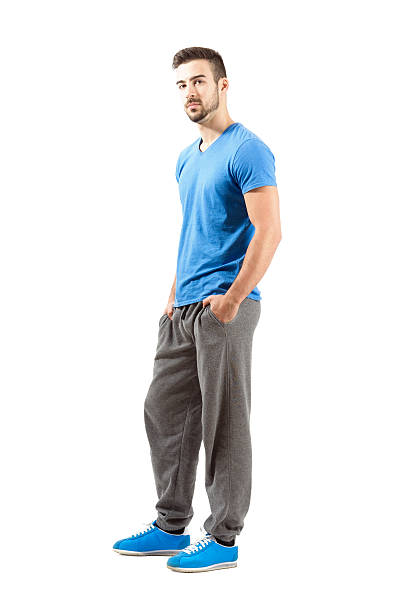 Side view of young guy in sportswear. Hands in pocket Side view of standing male in sportswear with hands in pocket. Full body length portrait isolated over white background. jogging pants stock pictures, royalty-free photos & images
