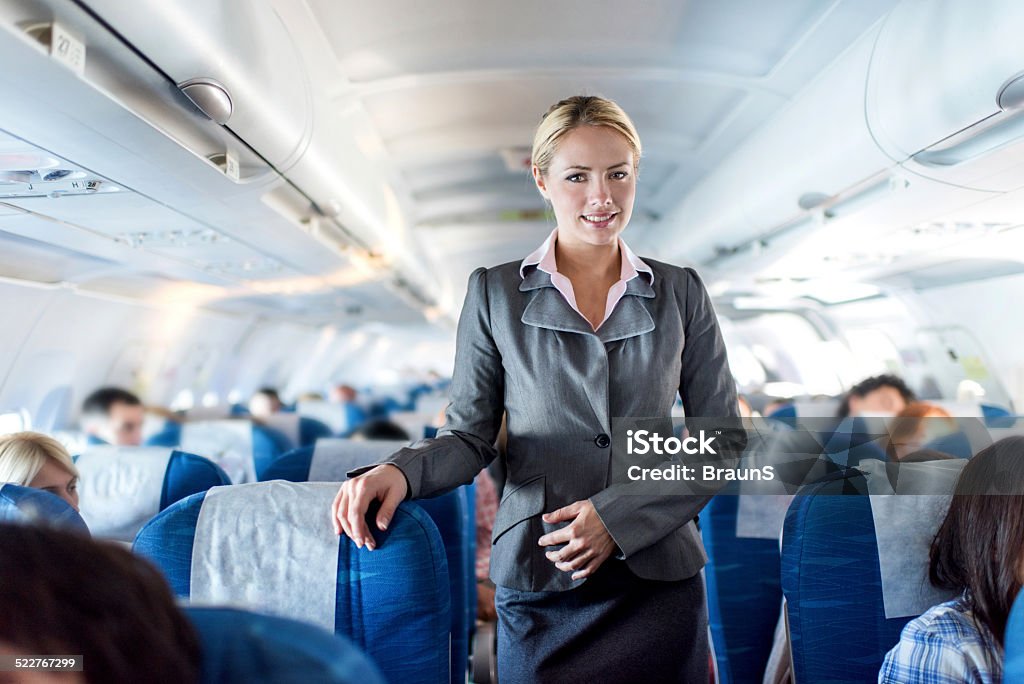 Flight attendant in airplane. Smiling female cabin crew standing in an airplane and looking at the camera. Air Stewardess Stock Photo