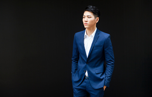 Candid portrait of a young well-built asian businessman. He looks like thinking heavily, analysing concepts and ideas in his mind, trying to foresee the future and what obstacles and opportunities it may bring. The man is wearing a blue luxurious suit and has a smooth hairstyle. Copy space available.