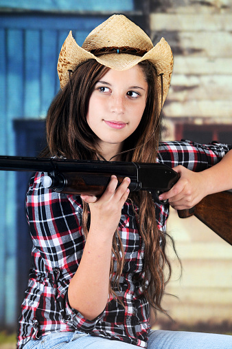 A pretty teen cowgirl taking aim with her rifle.
