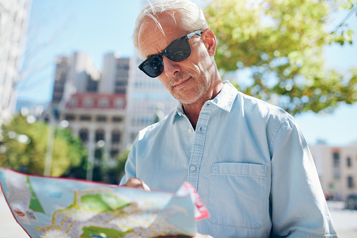 Senior man consulting a map while touring a foreign city. Mature caucasian man with sunglasses reading map for direction on summer day.