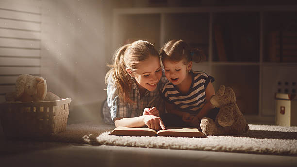 幸せな家族の母と娘読書での夜 - child bedtime imagination dark ストックフォトと画像
