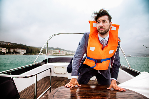 Businessman having a panic attack on his yacht during a storm. He is wearing his life vest and looking away as the storm approaches.