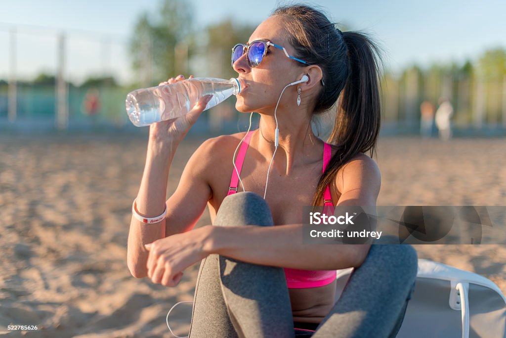 Beautiful fitness athlete woman drinking water after work out exercising Beautiful fitness athlete woman drinking water after work out exercising on sunset evening summer in beach outdoor portrait Accidents and Disasters Stock Photo