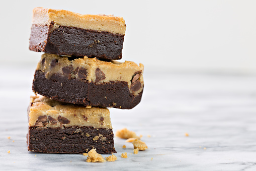 A close up photograph of a stack of three chocolate brookies a brookie is a brownie and chocolate chip cookie baked together and sliced into bars for eating.