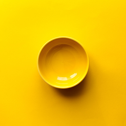New clean yellow bowl on yellow background. Top view