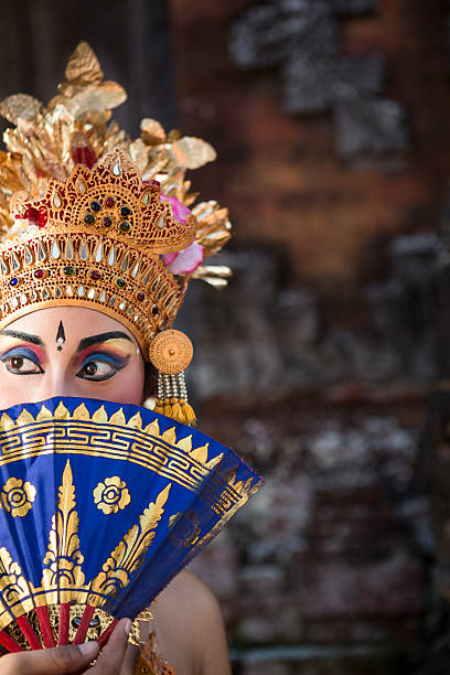 Ramayana Bali dancer with fan in a temple A young Bali female dancer is covering her face with a blue fan before entering stage of a theatrical Balinese performance in a temple location. With a selective focus on her brightly lit face, there is a nice copy space in the dark part of the image. ramayana stock pictures, royalty-free photos & images