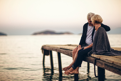 Loving senior couple enjoying the life and eachother, sitting on the dock by the seaside