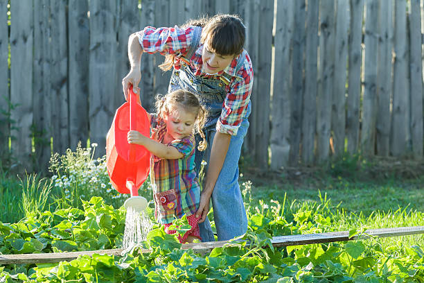 Piccolo Giardiniere ragazza aiutando la madre a versare orto letto - foto stock