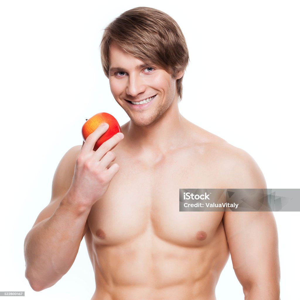 Young smiling bodybuilder holding apple. Portrait of young smiling bodybuilder holding apple in his hand - isolated on white background. Adult Stock Photo