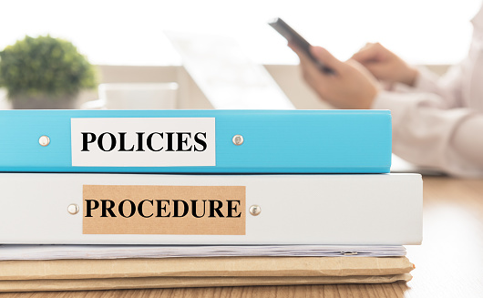Policies and Procedures doucuments place on desk in meeting room.  Policy, Procedure concept.