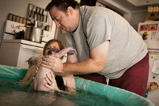 Father Taking Newborn from Birthing Tub During Home Water Birth Color photo of a father taking his newborn baby son from the water of a birthing tub immediately after he was born in a water birth at home. water birth photos stock pictures, royalty-free photos & images